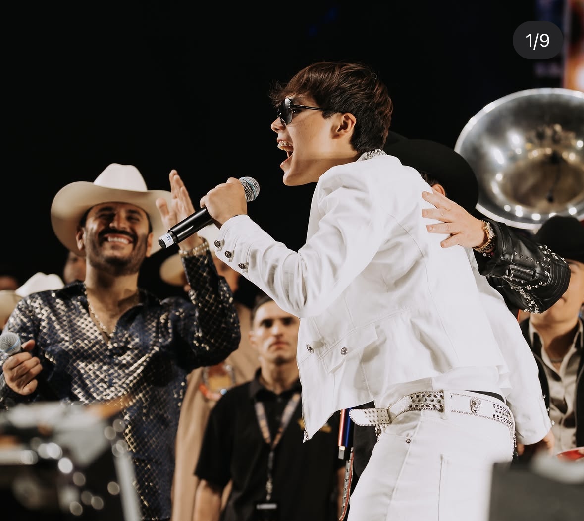 Bruno Caleb interpretando en vivo con chaqueta blanca y micrófono
